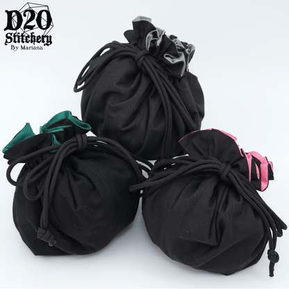 3 Epic dice bags with black exterior fabric, one with grey lining, one with green lining and one with pink lining tied with black paracord.