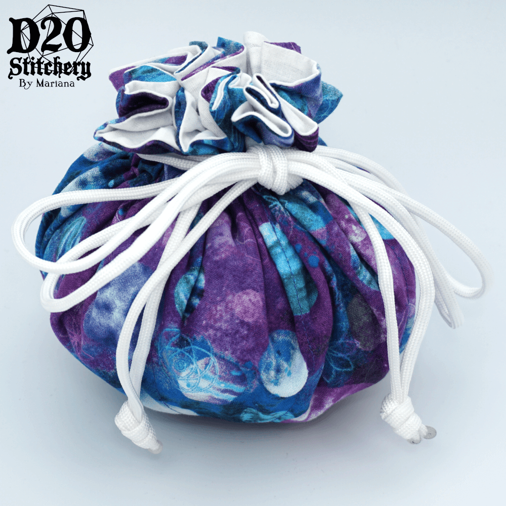 Epic dice bag with blue and purple planets on a mottled blue and purple background with white lining tied with white paracord.