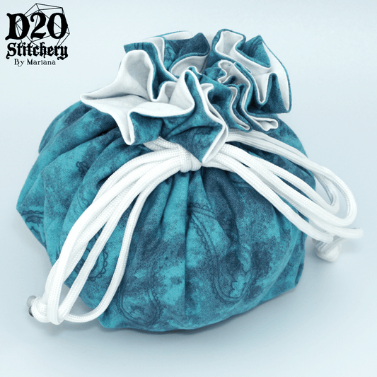 Epic dice bag with dark blue paisley outlines on a mottled medium and teal blue background tied with white paracord.